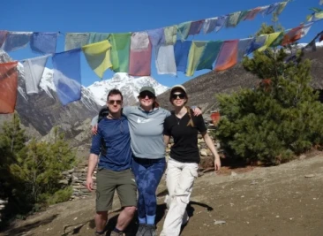 Friends posing under prayer flags with snowy mountains behind