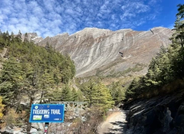 Mountain trekking trail sign under steep rocky peak