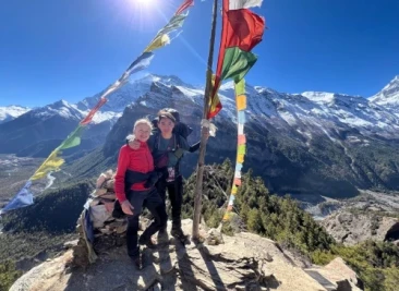 Trekkers at prayer-flag viewpoint above deep valley and snowy Annapurna peaks
