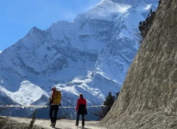 Two trekkers on narrow path below huge snowy mountain