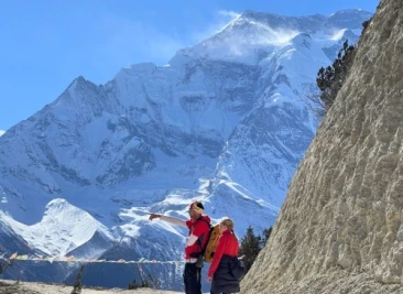 Two trekkers on snowy trail below towering Annapurna peak.
